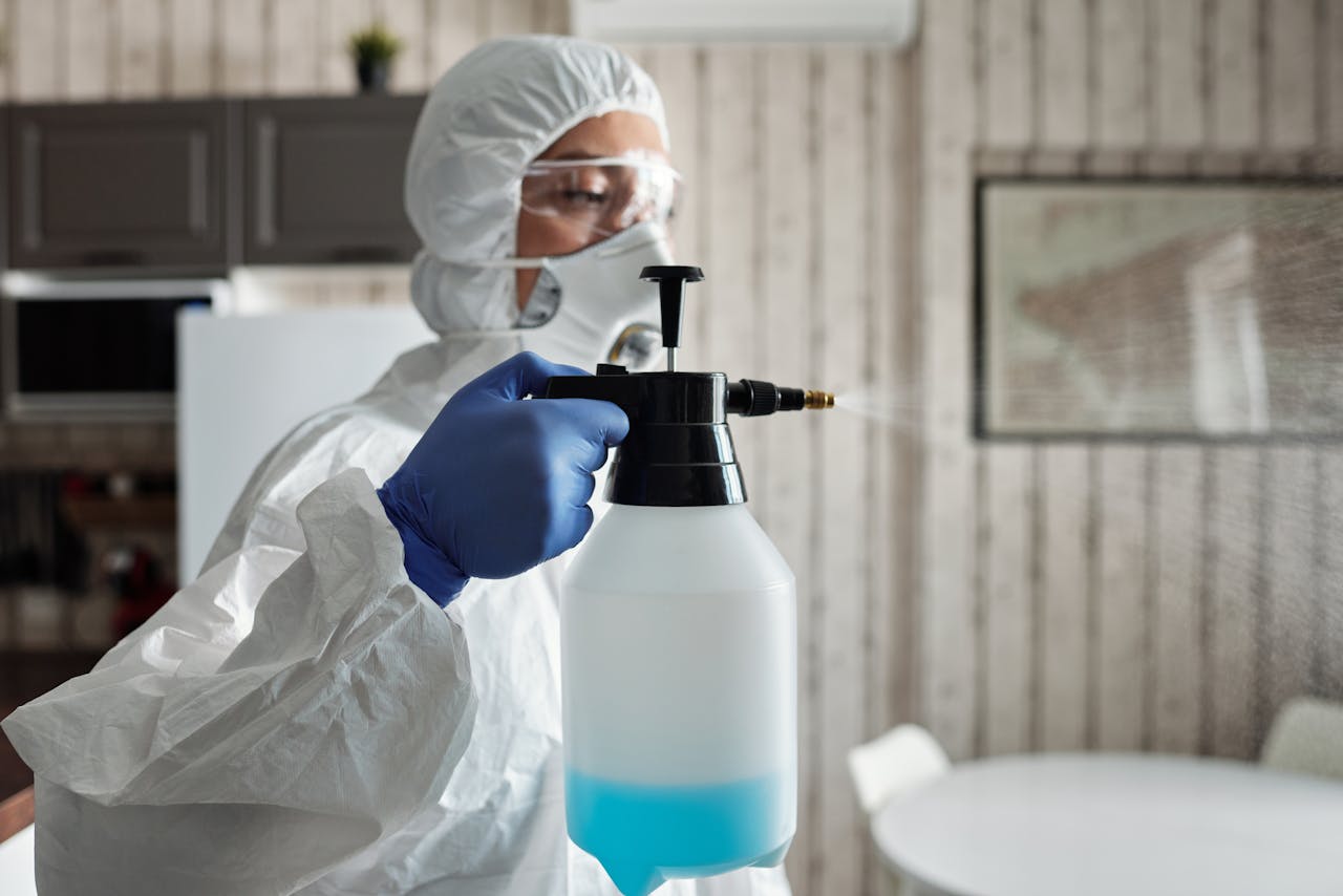 Professional in full gear disinfecting indoor area using a spray bottle for COVID-19 prevention.